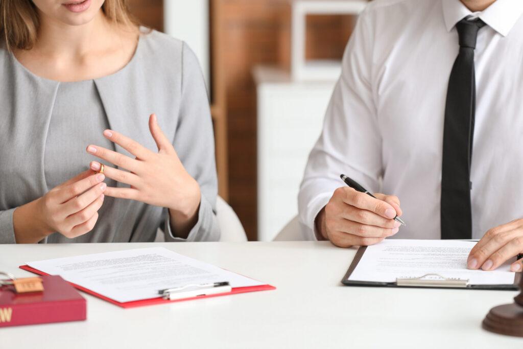 Close-up of a woman adjusting her wedding ring while sitting at a desk with a legal professional to sign official divorce papers.